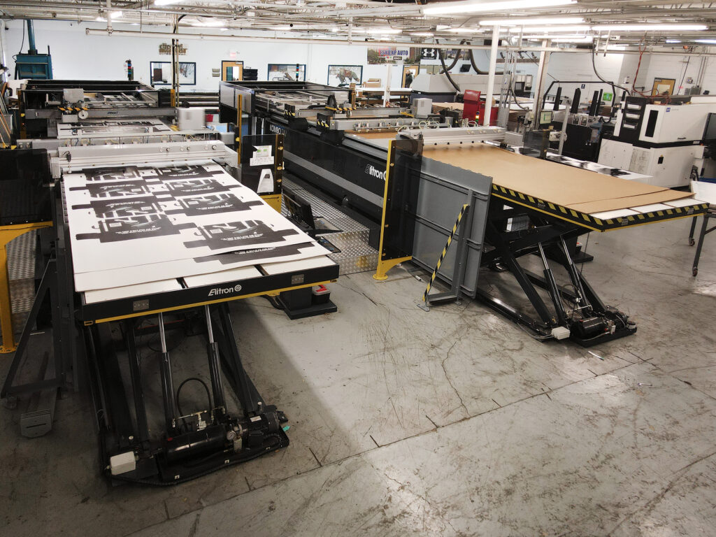 Digitally cut display sheets stacked on the unloading table beside an Elitron Kombo TAV-R die cutter at VT Group